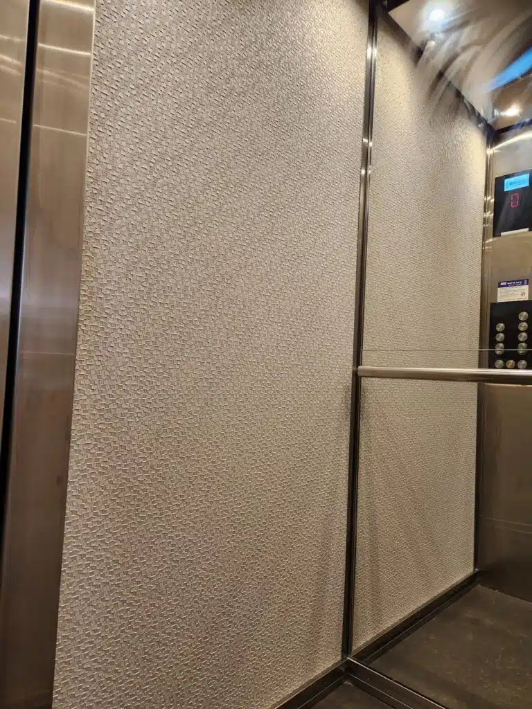 מעלית עם חיפוי קיר בעיצוב אריג בגוון בז׳ ומסגרות נירוסטה